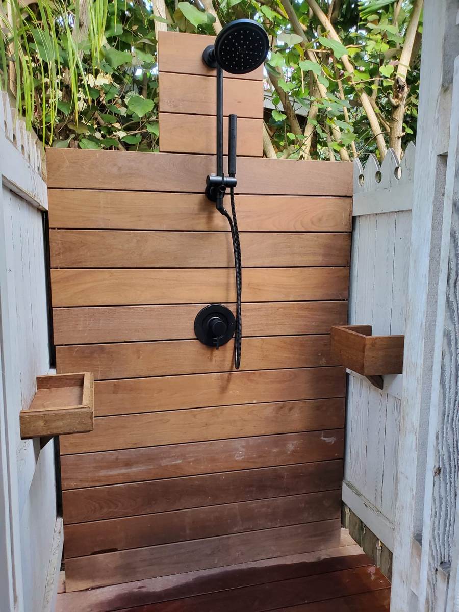 Outdoor shower clad in hardwood slats with black fittings.
