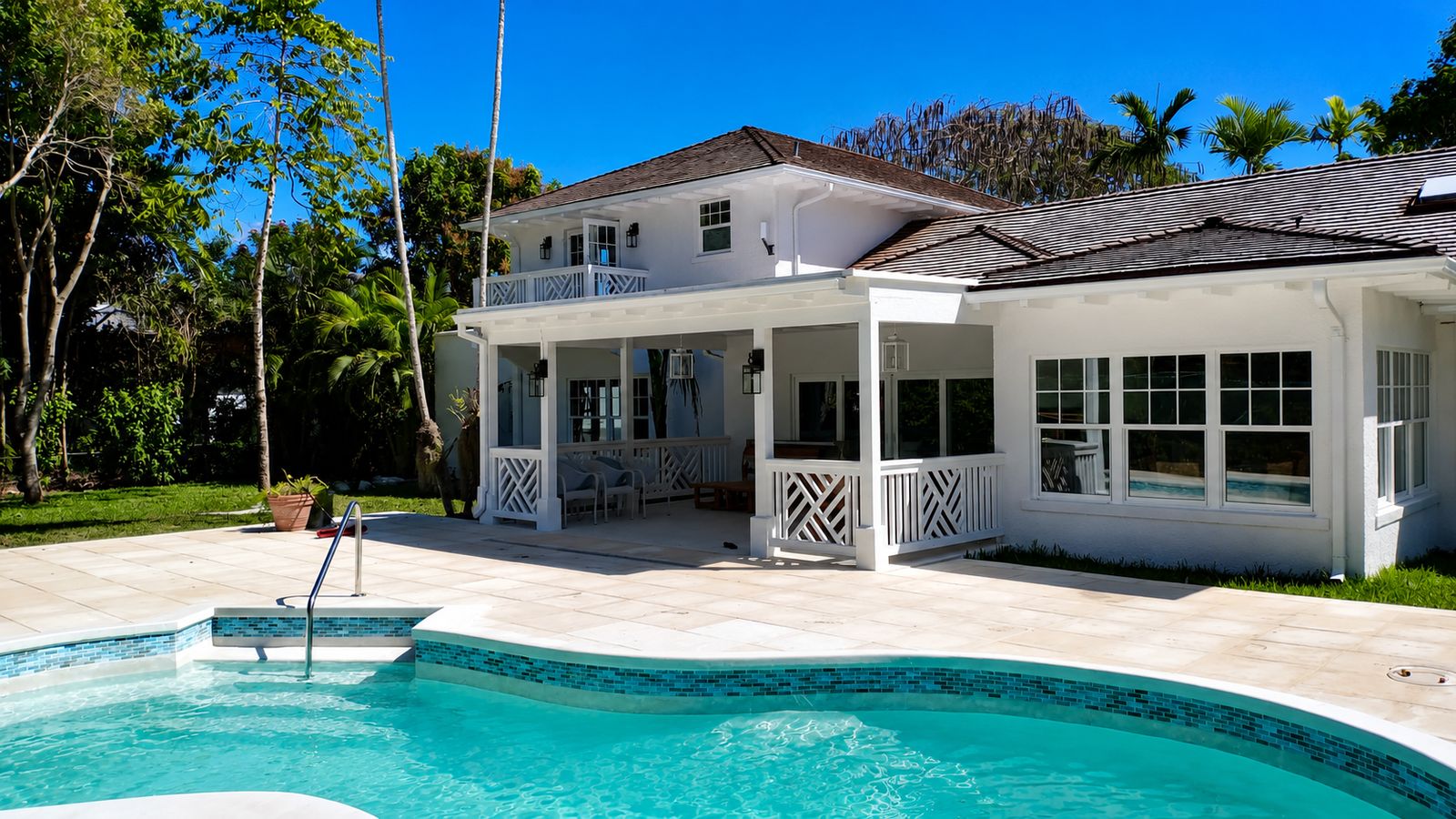 White home at Lyford Cay with covered veranda, chippendale railings and pool in the foreground.