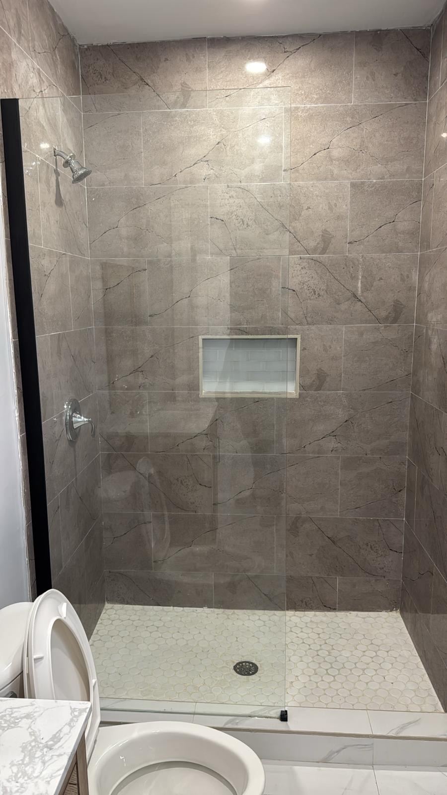 Shower finished in large format stone effect tile with a penny round floor.