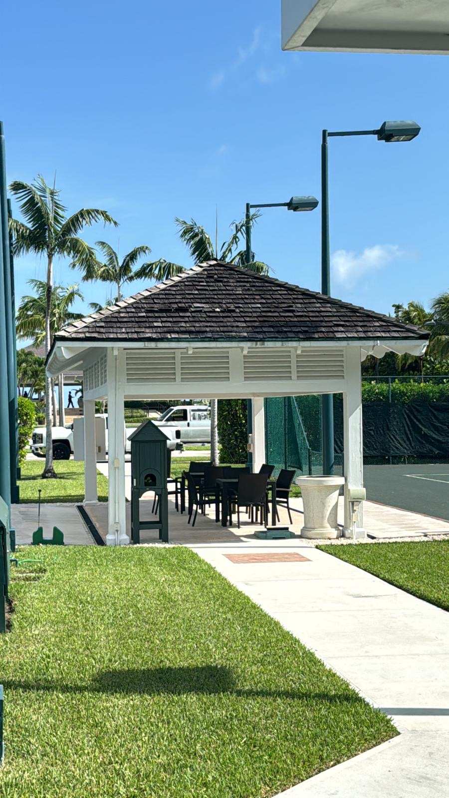 Shingled gazebo and manicured grounds beside a tennis court on a private estate.